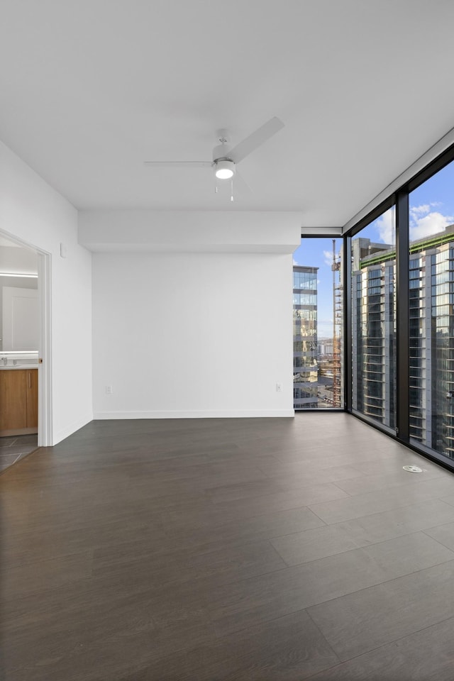 spare room featuring baseboards, a ceiling fan, a wall of windows, and dark wood finished floors
