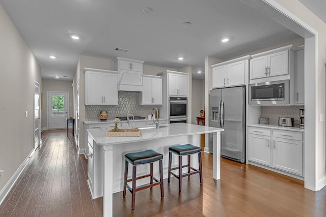 kitchen featuring appliances with stainless steel finishes, a sink, decorative backsplash, premium range hood, and dark wood finished floors