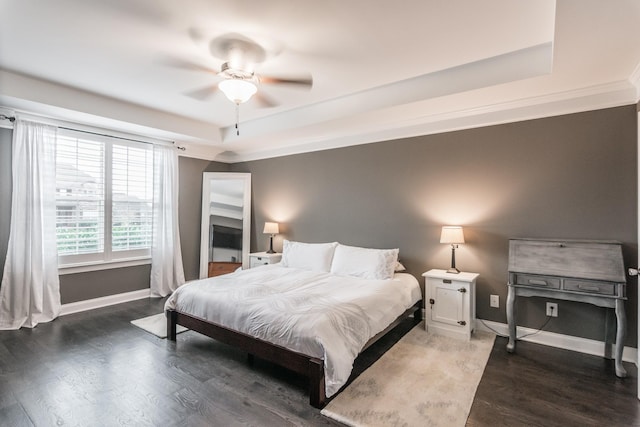 bedroom featuring a raised ceiling, wood finished floors, baseboards, and ceiling fan