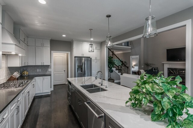 kitchen featuring appliances with stainless steel finishes, a sink, light stone counters, backsplash, and dark wood-type flooring
