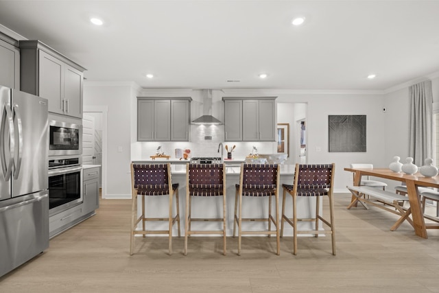 kitchen with gray cabinets, appliances with stainless steel finishes, wall chimney range hood, crown molding, and tasteful backsplash