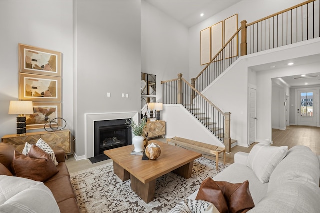 living room with a high ceiling, stairs, recessed lighting, baseboards, and a fireplace with flush hearth