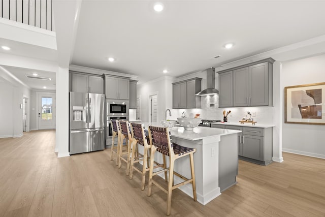 kitchen with stainless steel appliances, gray cabinetry, wall chimney exhaust hood, a kitchen island with sink, and recessed lighting