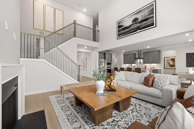 living room featuring a towering ceiling, light wood-type flooring, stairway, and recessed lighting