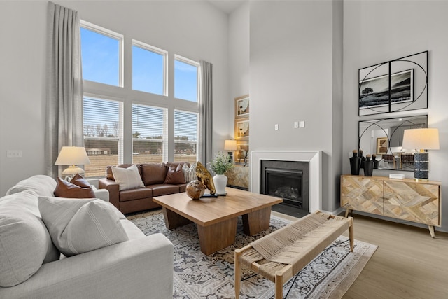 living room featuring a high ceiling, a glass covered fireplace, and light wood-type flooring