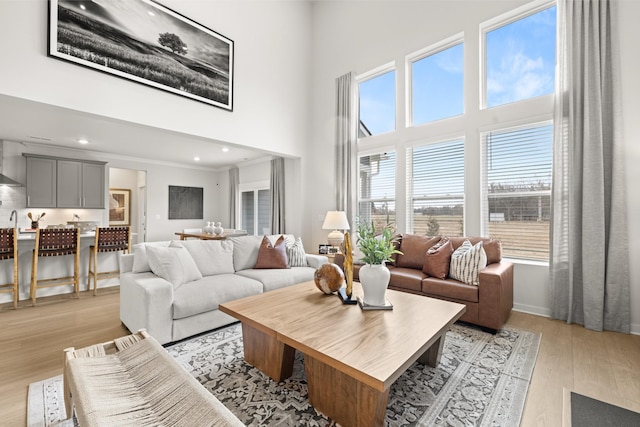 living area with light wood-style flooring, a towering ceiling, healthy amount of natural light, recessed lighting, and baseboards