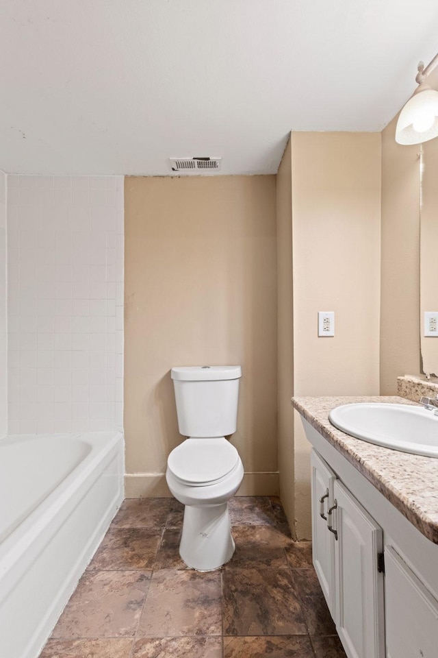 bathroom with vanity, toilet, stone finish flooring, a bath, and baseboards