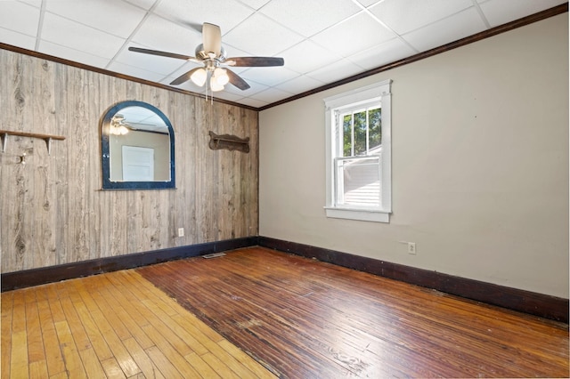 empty room with baseboards, wooden walls, crown molding, hardwood / wood-style floors, and ceiling fan