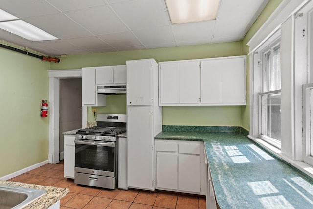 kitchen with stainless steel range with gas cooktop, under cabinet range hood, white cabinets, light tile patterned flooring, and a paneled ceiling