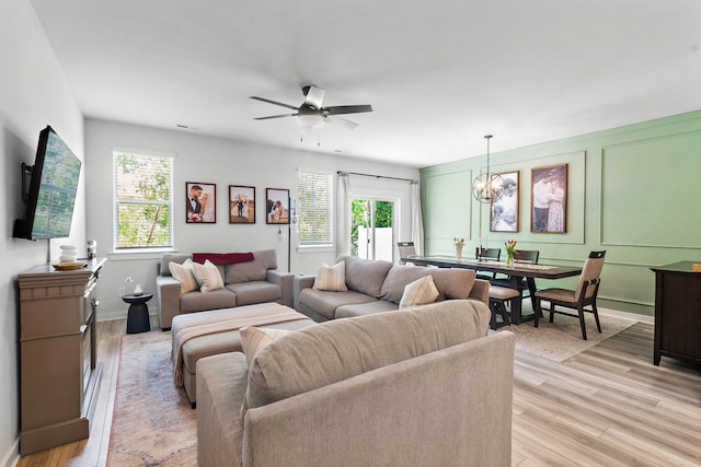 living area featuring light wood-type flooring, a chandelier, a ceiling fan, and baseboards