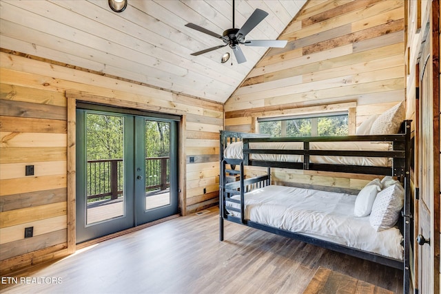 bedroom featuring vaulted ceiling, wooden walls, french doors, access to outside, and wood finished floors