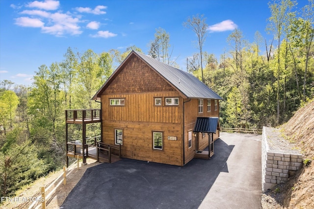 view of side of property featuring metal roof, fence, a wooden deck, and a view of trees