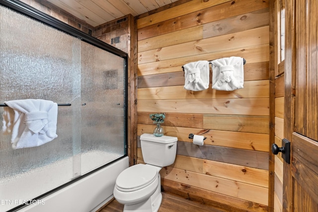 full bathroom with wooden walls, toilet, bath / shower combo with glass door, wood ceiling, and wood finished floors