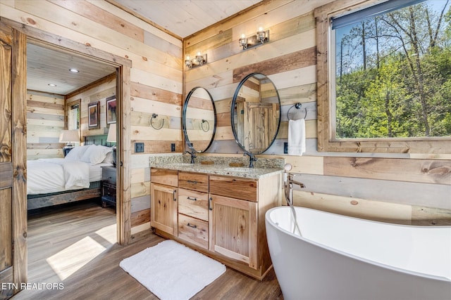 full bathroom featuring wood walls, ensuite bath, double vanity, wood finished floors, and a freestanding tub