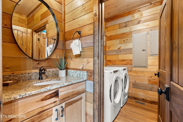 washroom featuring wood walls, light wood-style flooring, electric panel, independent washer and dryer, and wooden ceiling