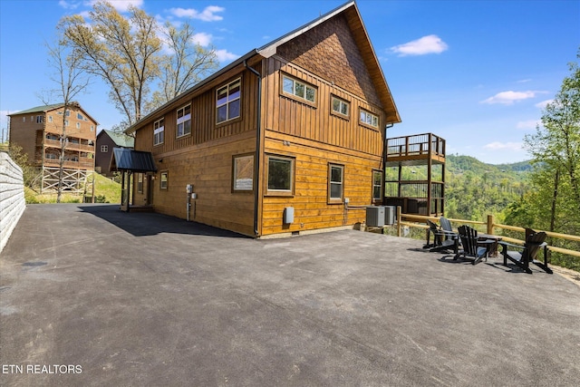 rear view of house featuring board and batten siding, central AC unit, and a patio