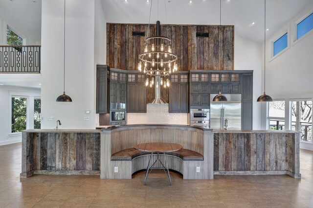 3910 Brick Church Pike, Nashville, TN 37207 - kitchen featuring a towering ceiling, stainless steel appliances, wall chimney range hood, a chandelier, and backsplash