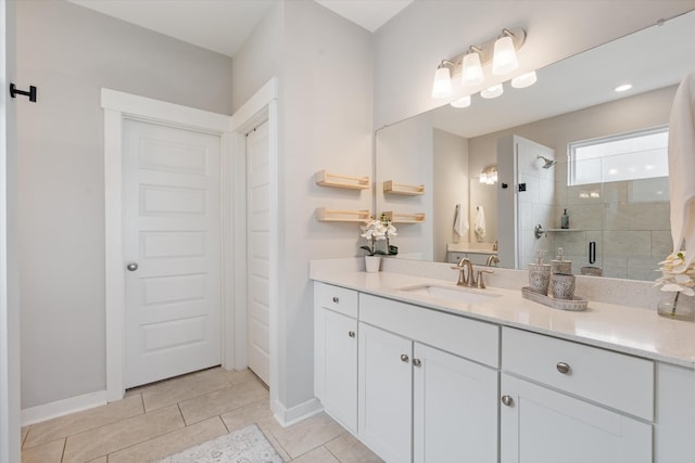 bathroom with a tile shower, vanity, tile patterned floors, and baseboards