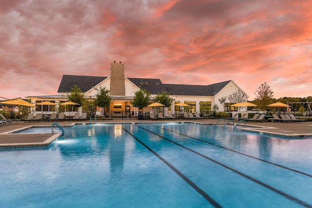 pool at dusk featuring fence, a community pool, and a patio area