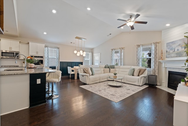 living area featuring vaulted ceiling, a ceiling fan, dark wood-type flooring, a premium fireplace, and a wainscoted wall