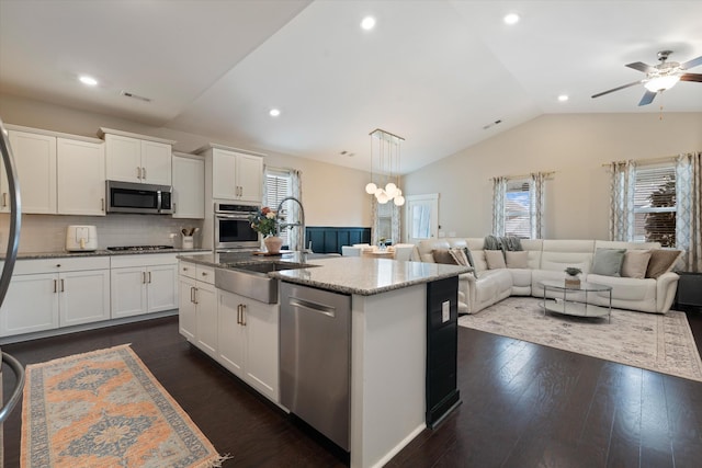 kitchen featuring appliances with stainless steel finishes, vaulted ceiling, a sink, plenty of natural light, and light stone counters