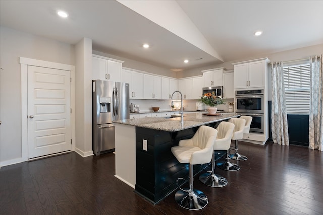 kitchen featuring stainless steel appliances, a sink, dark wood-type flooring, light stone countertops, and a kitchen bar
