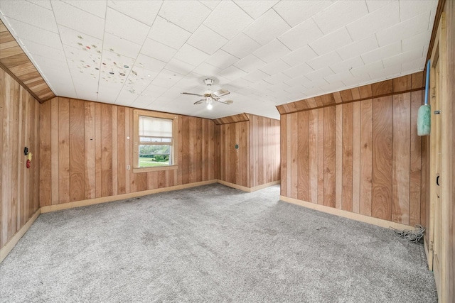 carpeted empty room with wood walls, ceiling fan, and baseboards