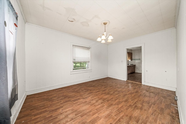 empty room featuring a chandelier, wood finished floors, baseboards, and ornamental molding