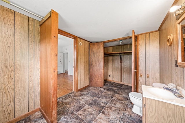 bathroom with wood walls, toilet, vanity, and baseboards