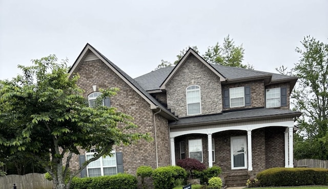 traditional home featuring brick siding, fence, covered porch, and a shingled roof