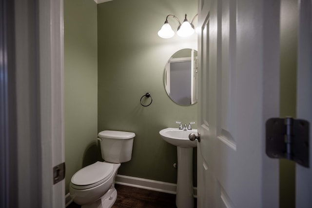 bathroom with baseboards, wood finished floors, toilet, and a sink