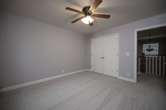 unfurnished bedroom with carpet flooring, baseboards, a closet, and a ceiling fan