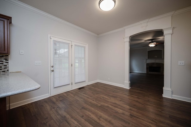 unfurnished dining area featuring ornate columns, a fireplace, ceiling fan, dark wood-type flooring, and crown molding