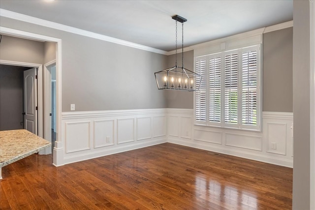unfurnished dining area featuring a chandelier, a wainscoted wall, dark wood finished floors, and ornamental molding