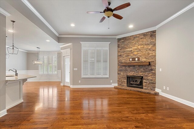 unfurnished living room with ceiling fan, ornamental molding, wood finished floors, a sink, and a stone fireplace