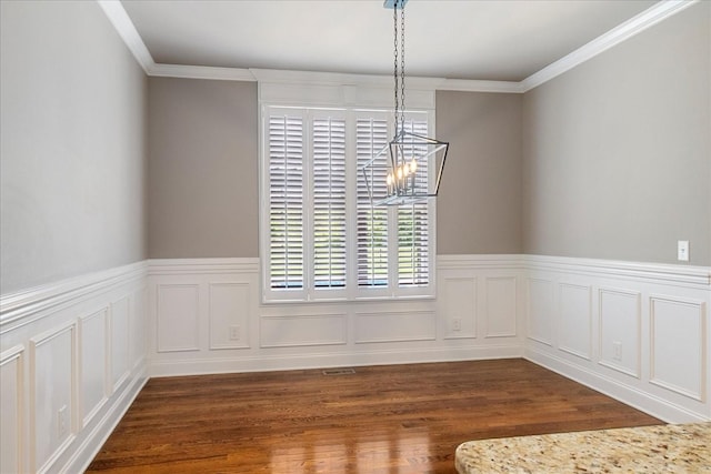 unfurnished dining area with dark wood finished floors, ornamental molding, a wainscoted wall, and a chandelier