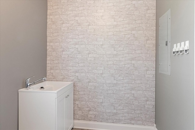 bathroom featuring a sink, brick wall, baseboards, and electric panel