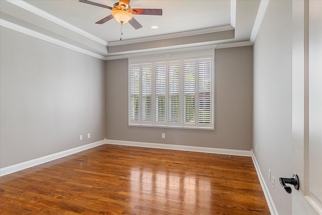 unfurnished room with a raised ceiling, crown molding, ceiling fan, wood finished floors, and baseboards