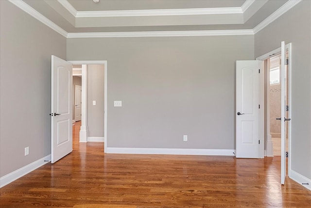 empty room featuring wood finished floors, ornamental molding, a raised ceiling, and baseboards