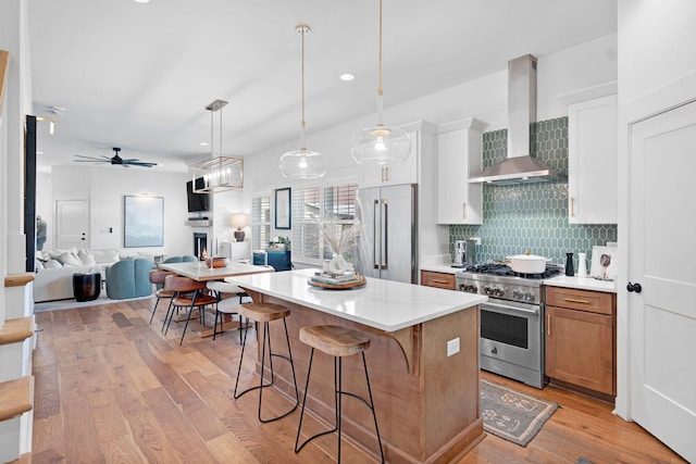kitchen with high end appliances, wall chimney exhaust hood, backsplash, light wood-style flooring, and a breakfast bar area