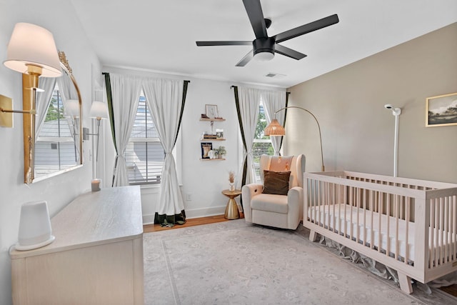 bedroom featuring a nursery area, a ceiling fan, baseboards, and wood finished floors