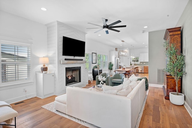living area with a ceiling fan, a fireplace, light wood-type flooring, baseboards, and recessed lighting