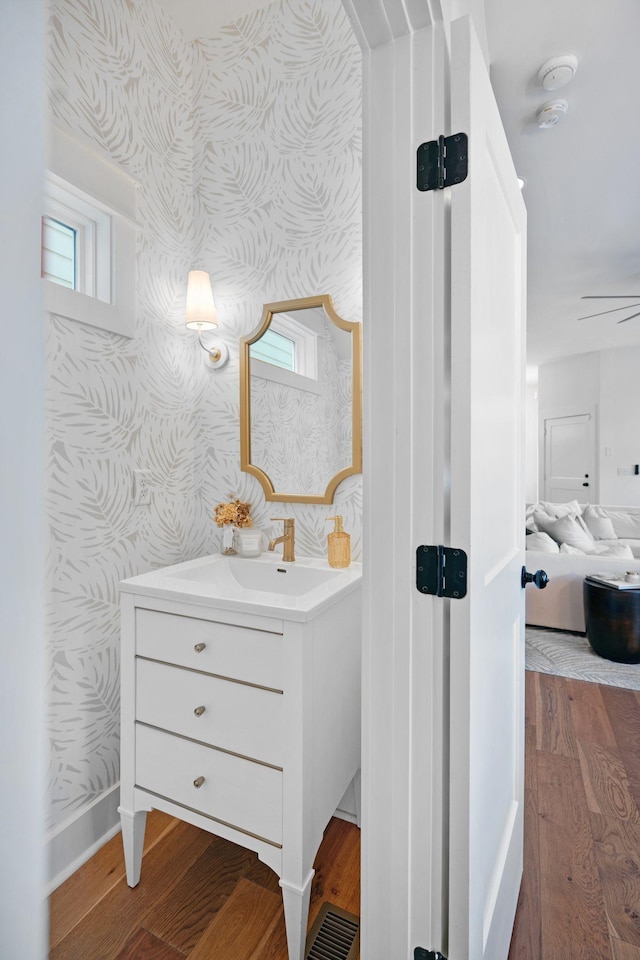 bathroom with wallpapered walls, wood finished floors, baseboards, and vanity