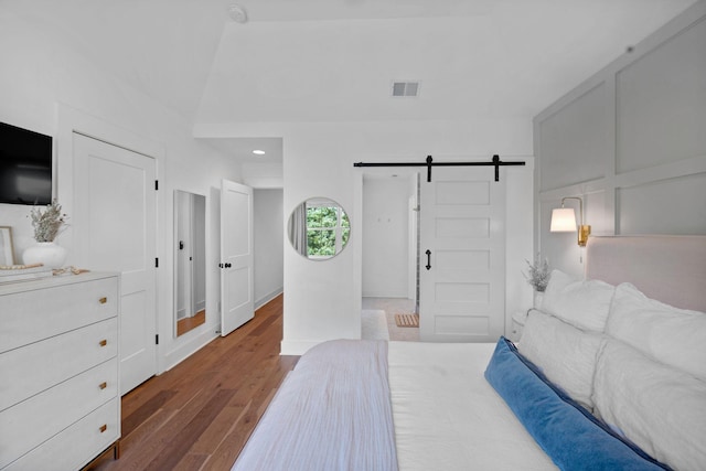 bedroom with a barn door, wood finished floors, recessed lighting, and baseboards