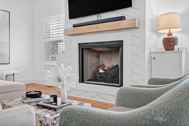living room featuring wood finished floors, a warm lit fireplace, and baseboards