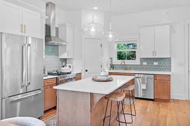 kitchen featuring appliances with stainless steel finishes, wall chimney exhaust hood, a sink, light wood-style floors, and light countertops