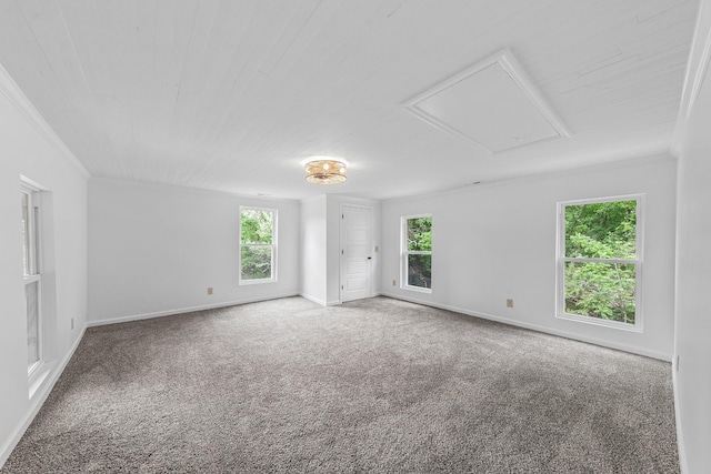 carpeted empty room with attic access, baseboards, and crown molding