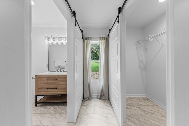 walk in closet featuring a barn door, light marble finish floors, and a sink
