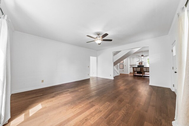 unfurnished living room with ceiling fan, stairway, dark wood-type flooring, baseboards, and ornamental molding
