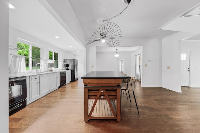 kitchen featuring black appliances, white cabinets, wood finished floors, a sink, and crown molding
